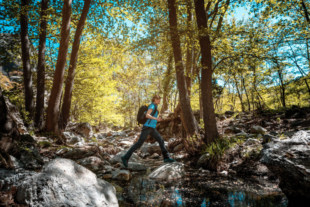 Active woman hiking jumping over a creek in spring, Serres, Central Macedonia Greece