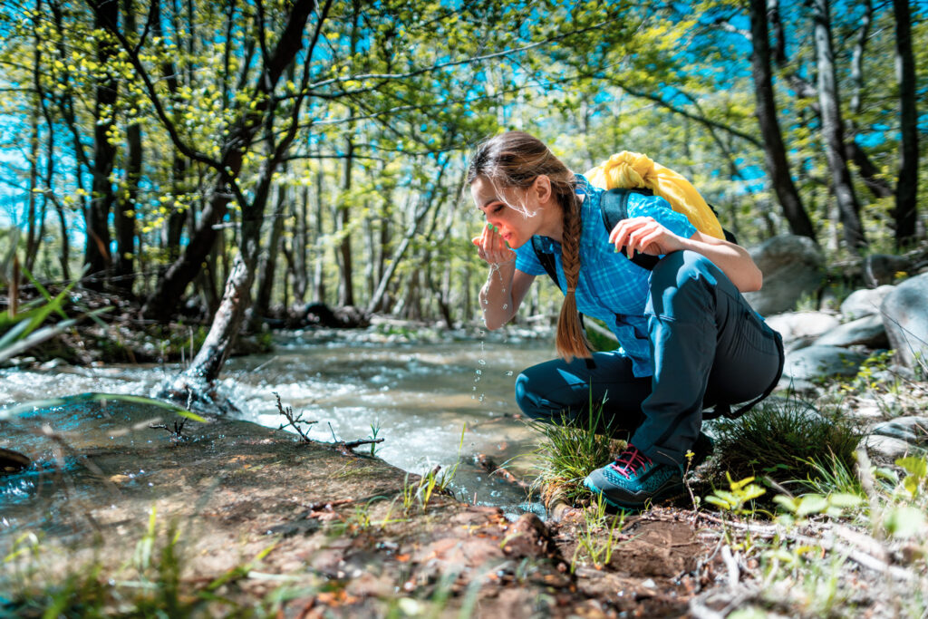 Woman refreshing herself with fresh water from clear creek while hiking, Serres, Central Macedonia Greece
